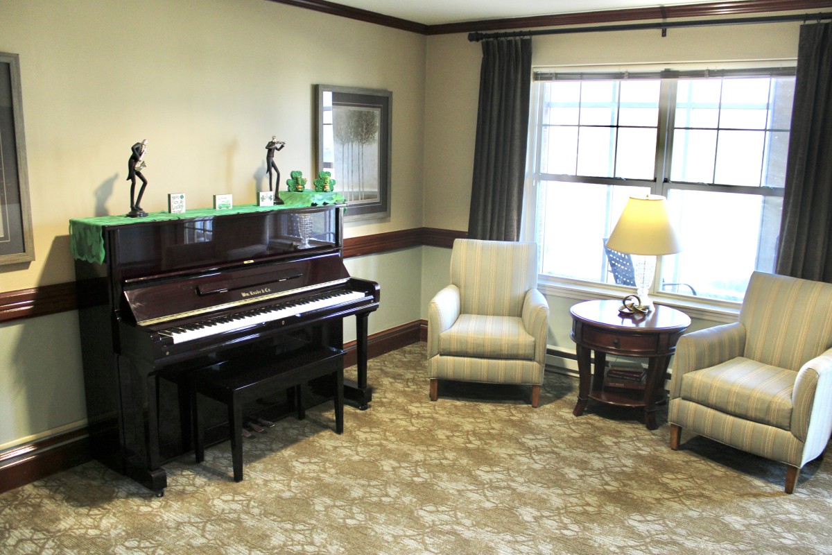 A cozy living room with a piano, armchair, and a lamp by the window.