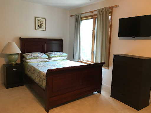 A cozy and well-furnished bedroom featuring a wooden bed, natural light from the window, and a mounted television.