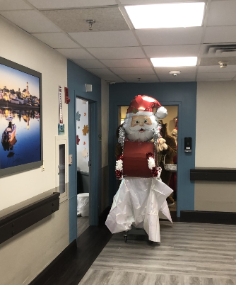 A festive figure dressed as Santa Claus walking through a hospital corridor, spreading holiday cheer.