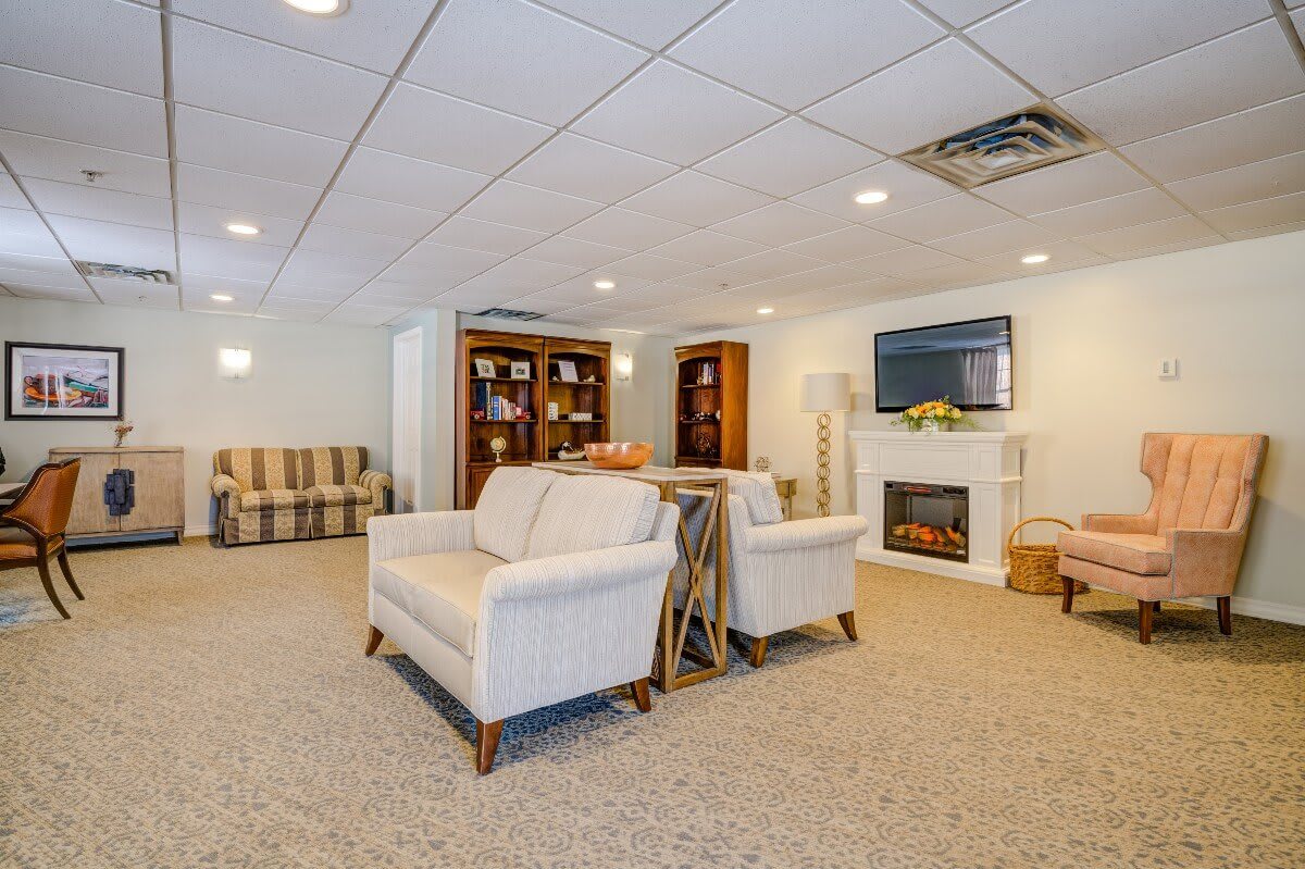 A cozy living room with beige sofas, armchairs, a fireplace, and a TV, complemented by bookshelves and warm lighting.