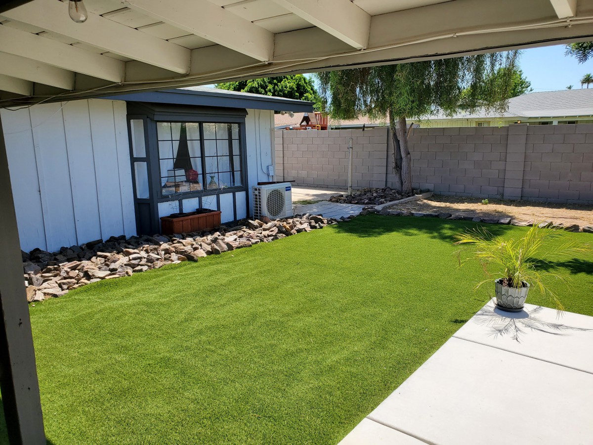 A modern backyard with artificial grass and clean landscaping under a shaded patio.