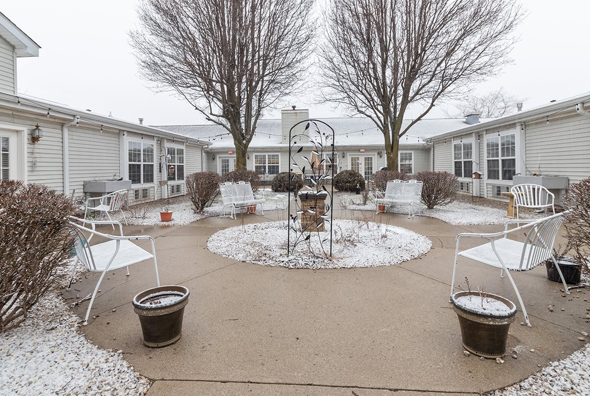 A snowy courtyard with trees, benches, and a central decoration.