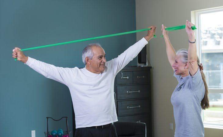 An elderly couple exercises with a resistance band at home.