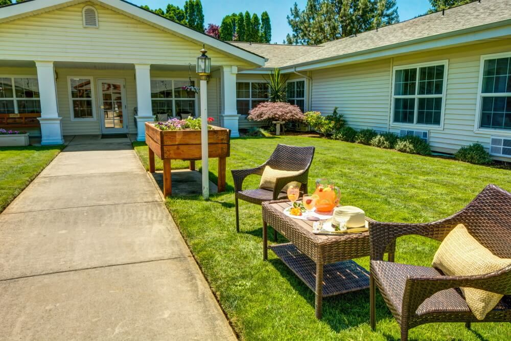 A cozy outdoor patio setup with a table and chairs on a lawn in front of a house.