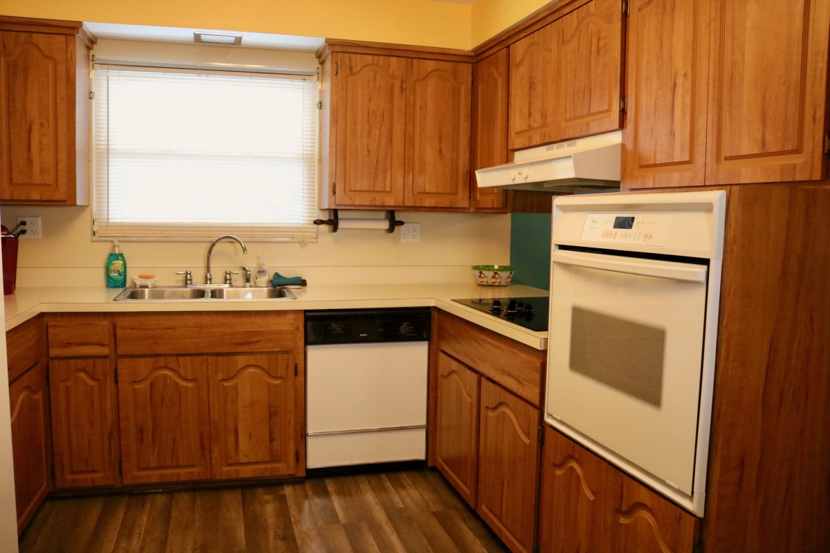 A cozy kitchen with wooden cabinets, an oven, a dishwasher, and a window.