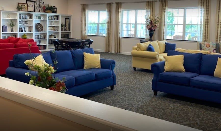 A cozy living room featuring a blue sofa, yellow armchair, and large windows with curtains.