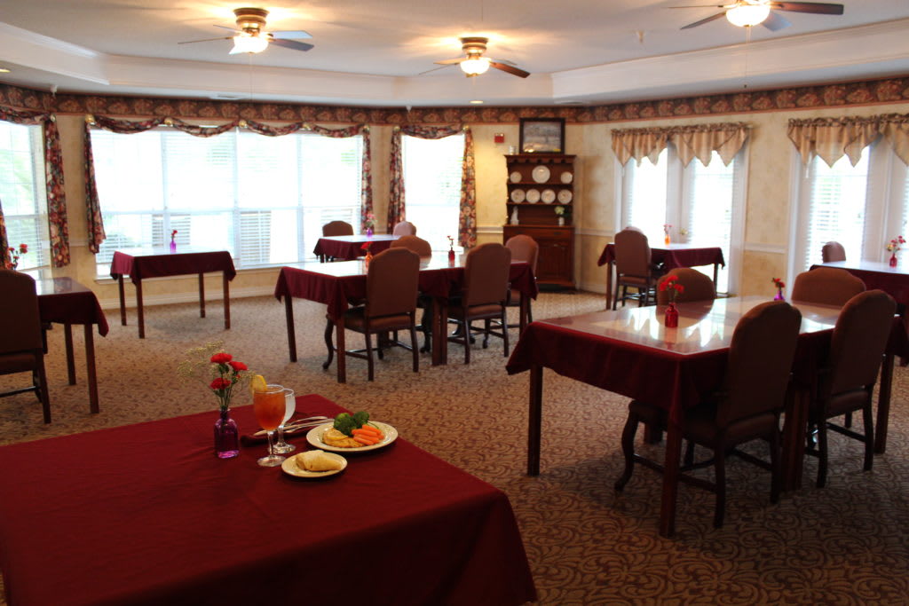 A cozy dining room with maroon tablecloths and neatly arranged tables and chairs.