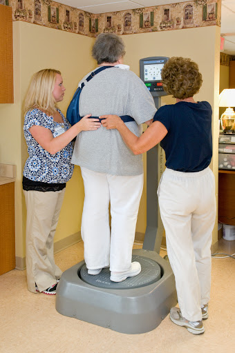 Two healthcare professionals assist a patient on a balance or body composition scale.