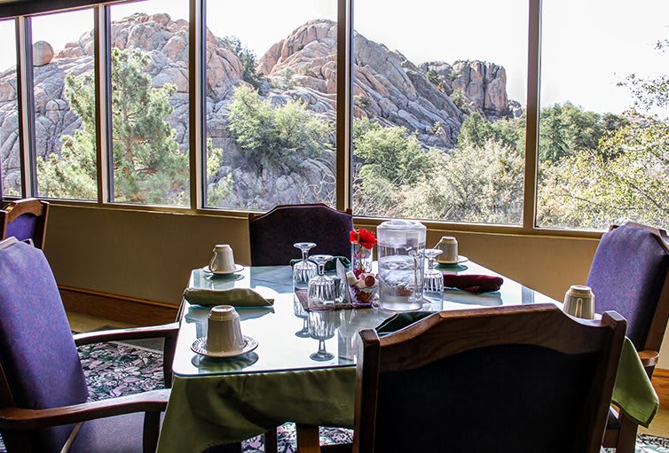 A dining table is set with plates and glasses, overlooking a scenic view of rocky landscapes through large windows.