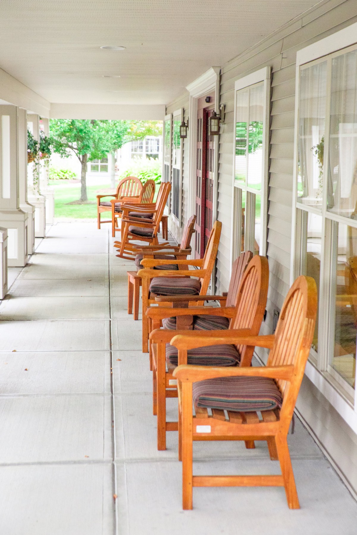 A row of wooden chairs with cushions lined up on a sunny porch.