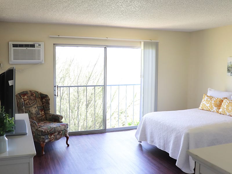A minimalist bedroom with natural light and a small seating area.