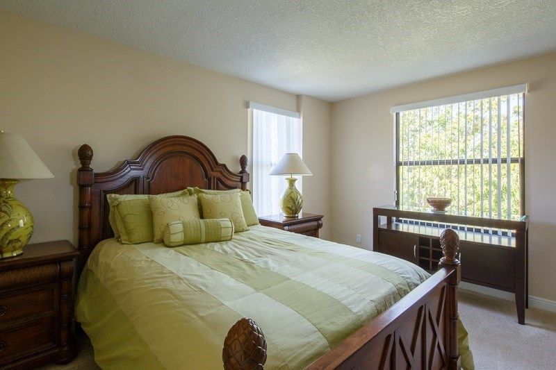 A cozy bedroom with a wooden bedframe, green bedding, and natural light from two windows.