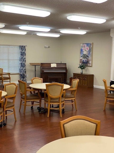 A community dining area with several round tables, chairs, and a piano in the corner.