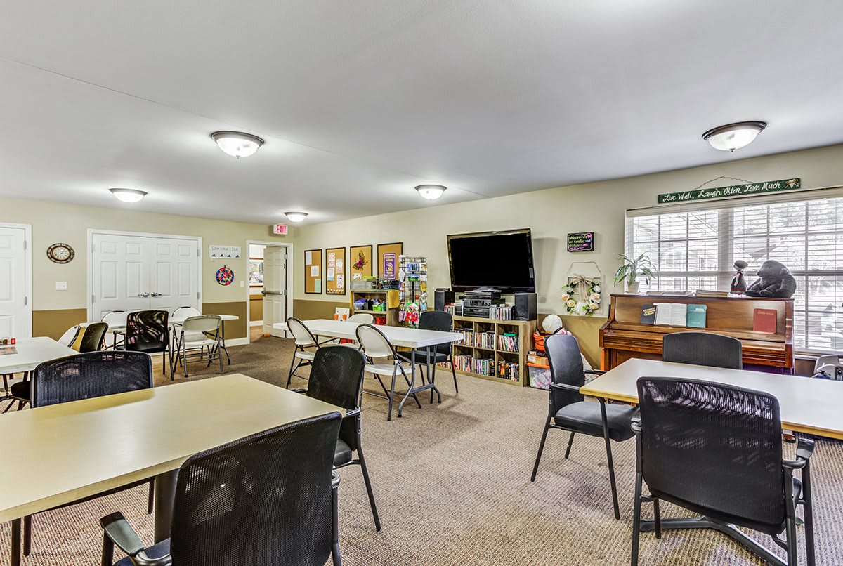 A community room with several tables and chairs, a television, and a piano.