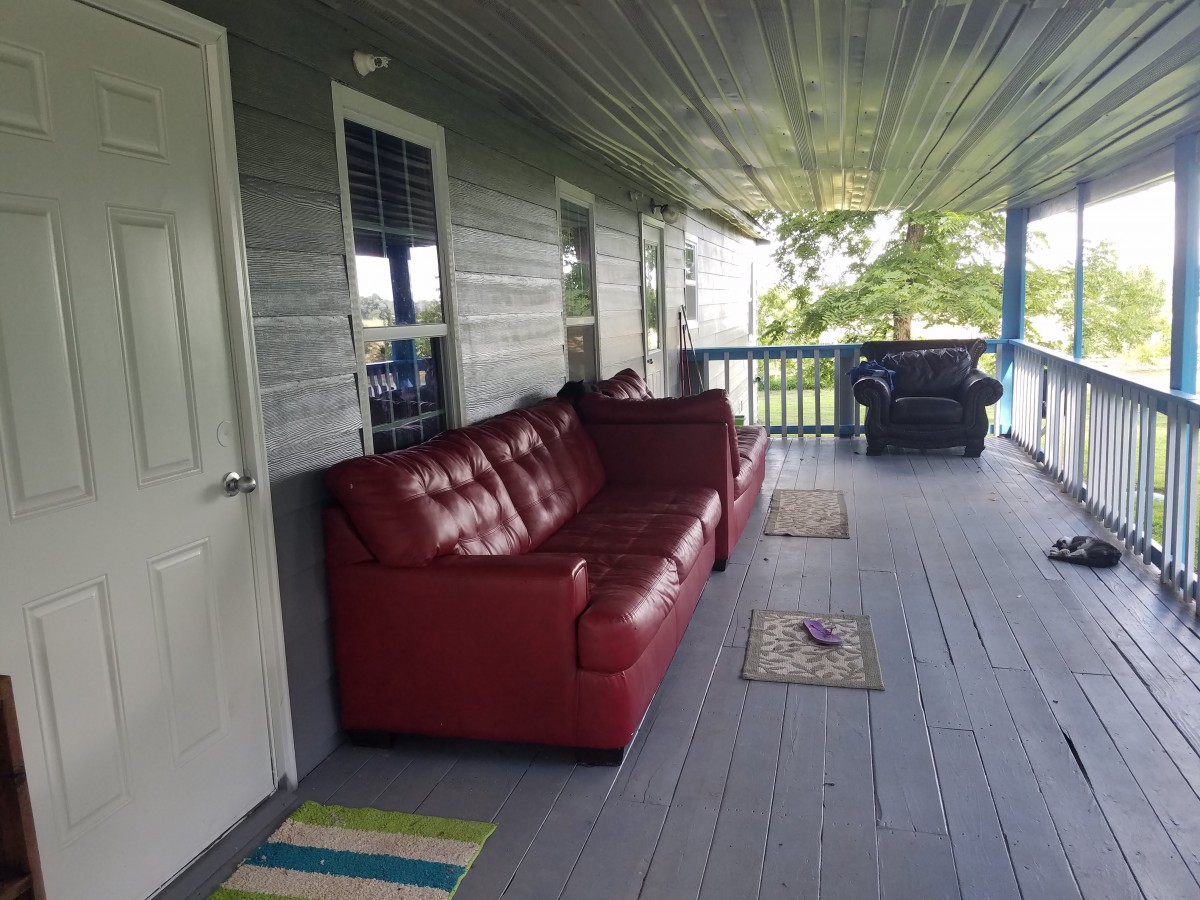 A cozy porch with a red sofa and rugs on a wooden floor.