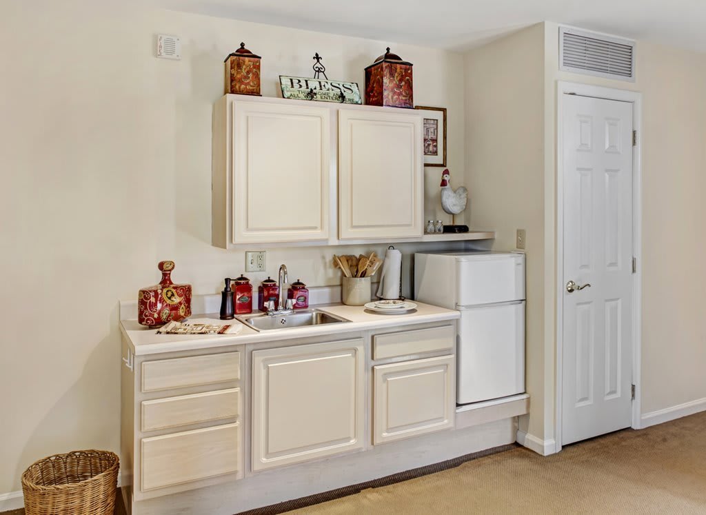 A kitchen area featuring white cabinets, a countertop with decorative jars, and a small fridge.