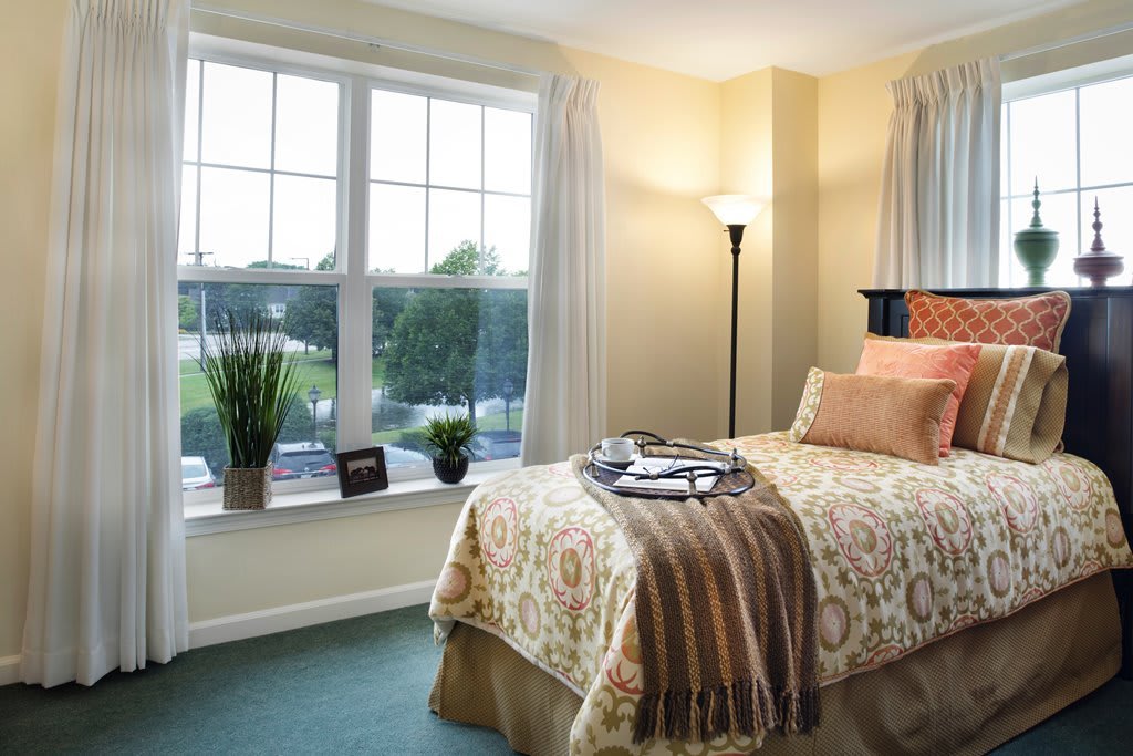 A cozy bedroom with a single bed, large windows, and natural lighting.