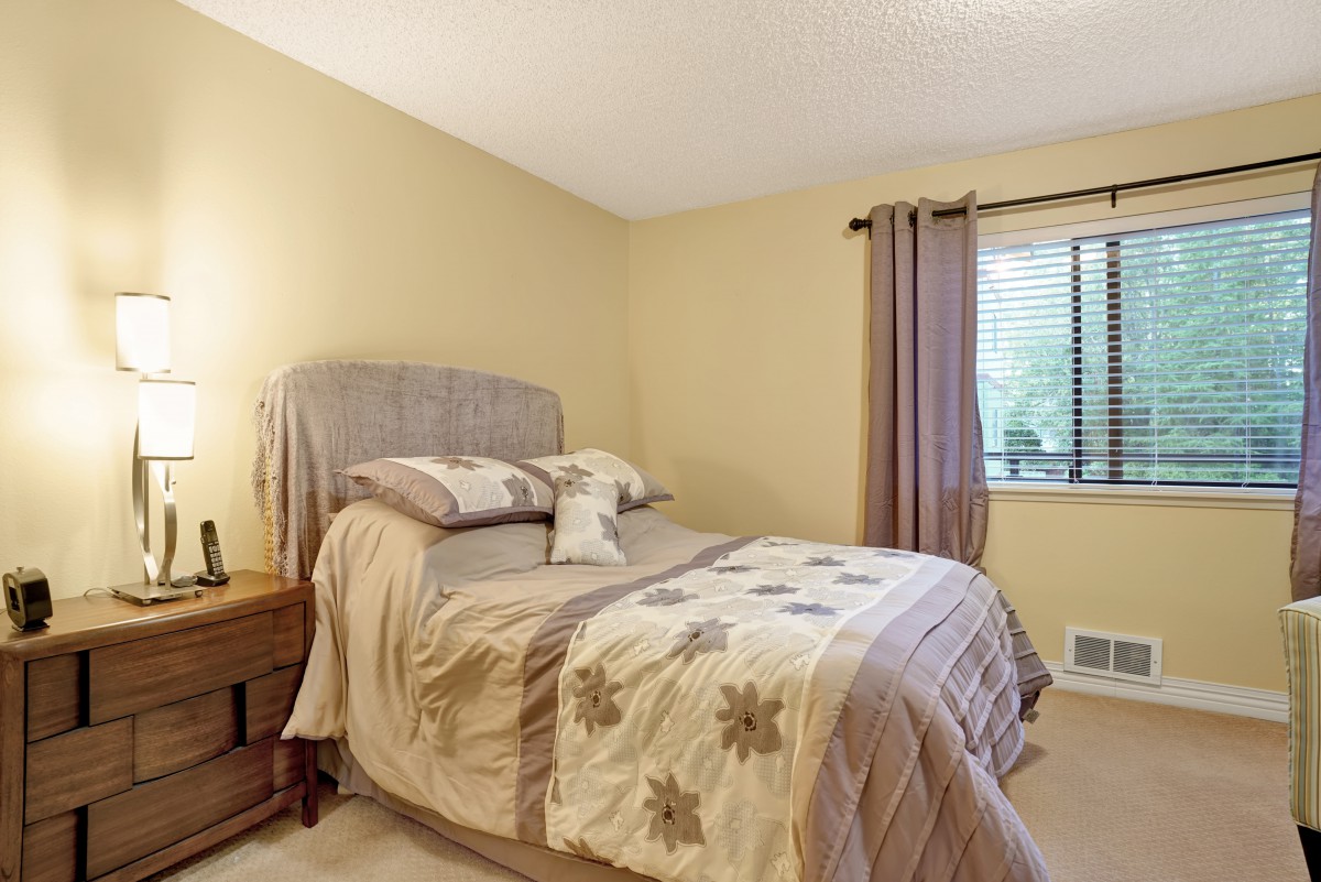 A cozy bedroom with a neatly made bed, soft lighting, and a window with curtains.