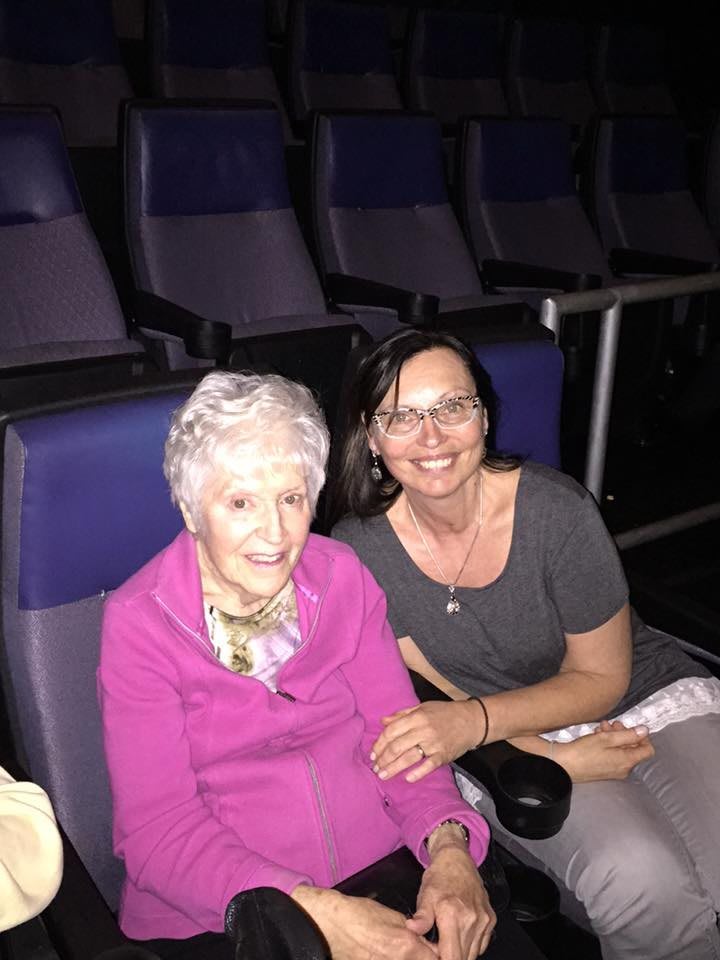 Two people sitting in cinema seats, smiling at the camera.