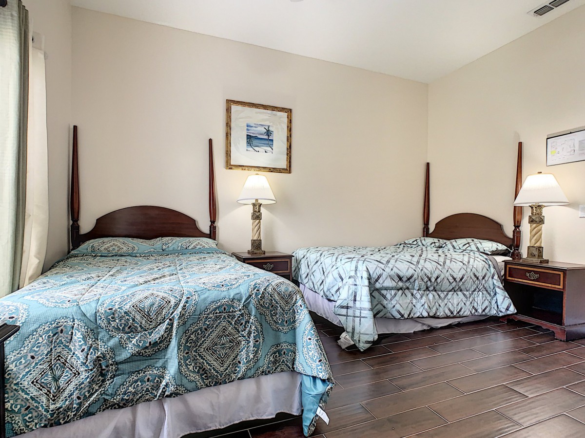A cozy bedroom featuring two beds with patterned bedspreads, a lamp on a nightstand, and a painting on the wall.