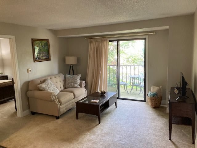 A cozy living room with a sofa, coffee table, and lamp next to a sliding glass door leading to a balcony.