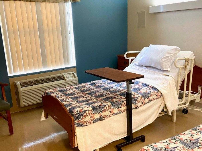 A hospital room with a neatly made bed and an adjustable overbed table.