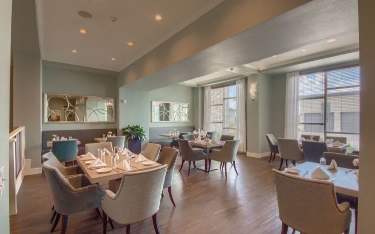 An elegant restaurant interior with well-arranged dining tables and chairs, accentuated by natural light from large windows.