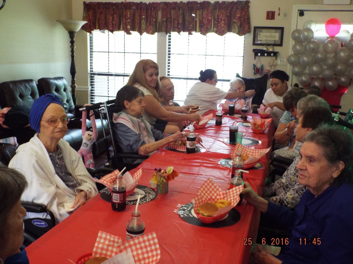 A group of people gathered around a dining table for a celebration, with food and drinks on the red tablecloth.
