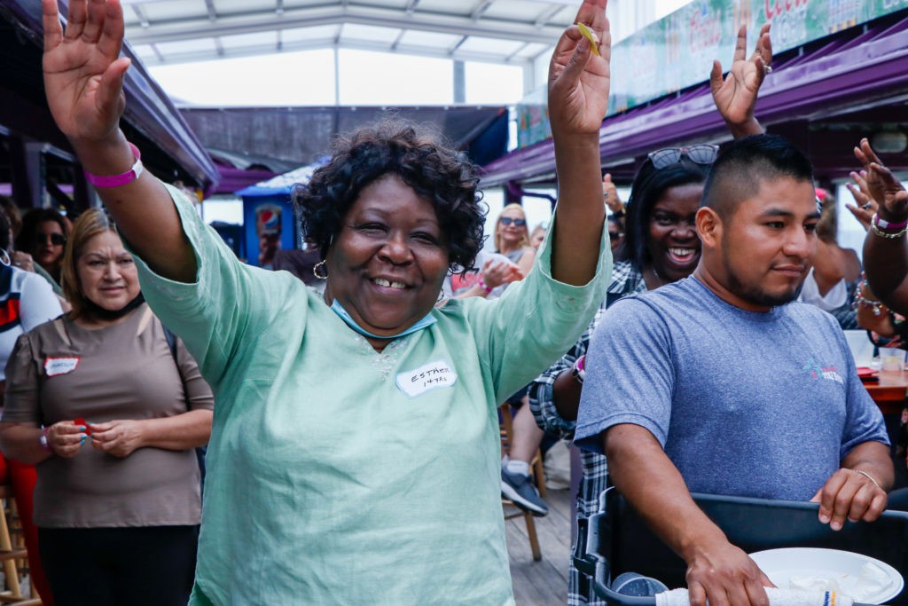 A joyful group of people celebrating outdoors with smiles and raised hands.