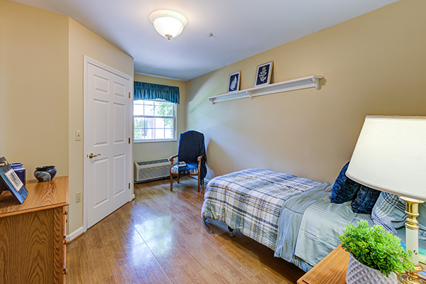 A cozy bedroom with a single bed, wooden flooring, and a window letting in natural light.