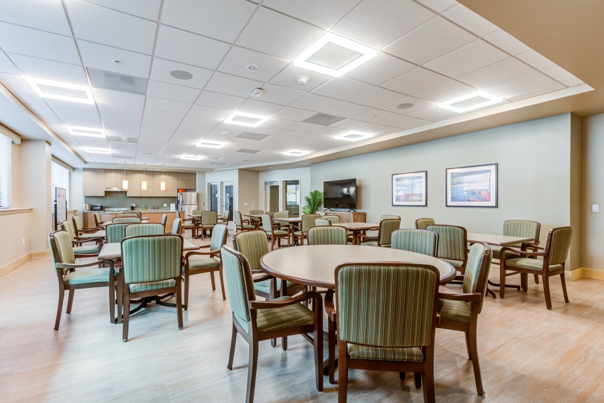 A spacious dining area with multiple tables and chairs, featuring modern lighting and a television on the wall.
