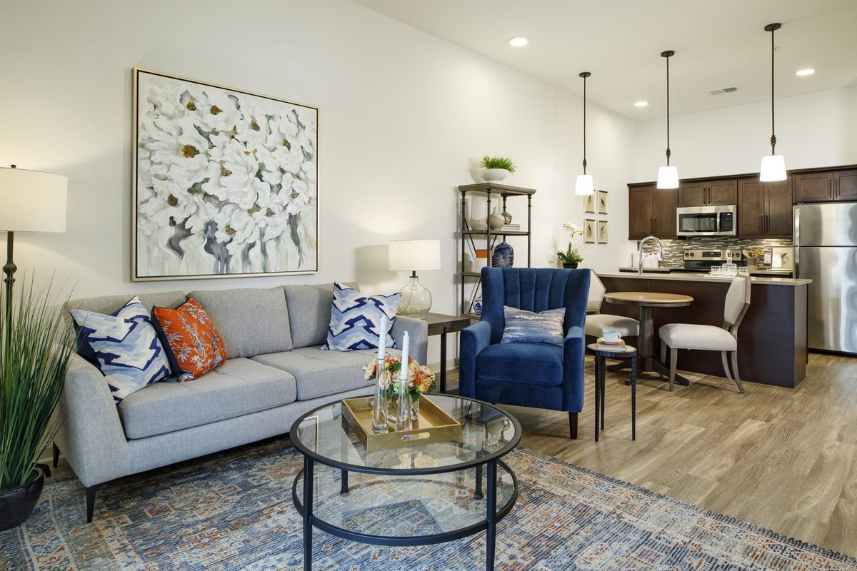 A modern living room with stylish furniture and decor, featuring a cozy gray sofa, elegant blue chair, and a glass coffee table in an open-concept space.