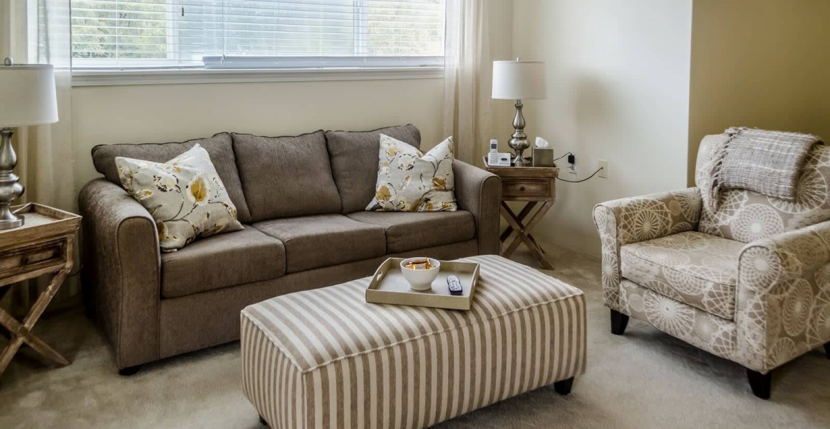 A cozy living room with a brown sofa, patterned ottoman, and decorative accents.