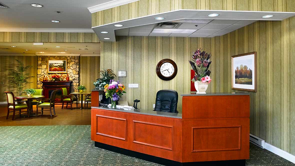 A reception desk with floral arrangements and a wall clock in a lobby setting.