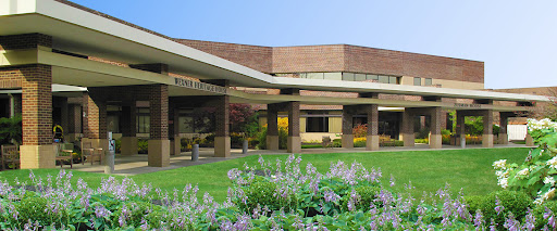A view of a medical facility featuring modern architecture, surrounded by lush greenery and colorful flowers.
