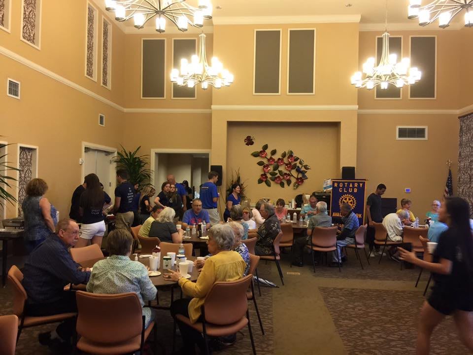 A social event with people seated at tables in a well-lit room featuring chandeliers and wall decorations.
