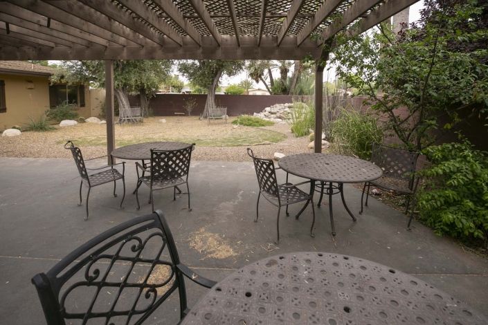 A covered patio with metal tables and chairs in a backyard setting.