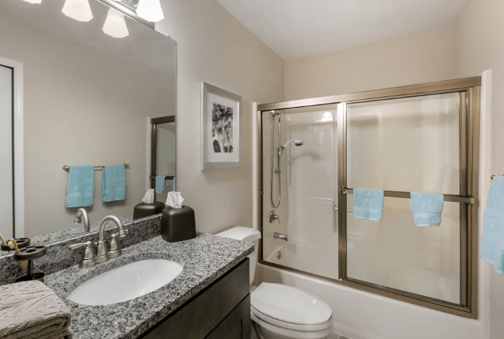 A modern bathroom with a granite countertop, shower enclosure, and neatly hung towels.