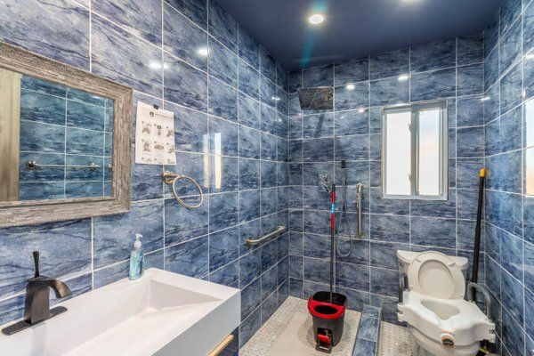 A modern bathroom with blue tiled walls, featuring a sink, mirror, and toilet.