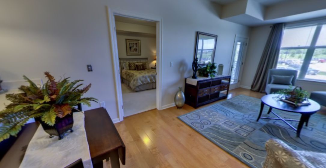 A cozy living room with hardwood floors, decorated with a large rug and stylish furniture, leading into a bedroom.
