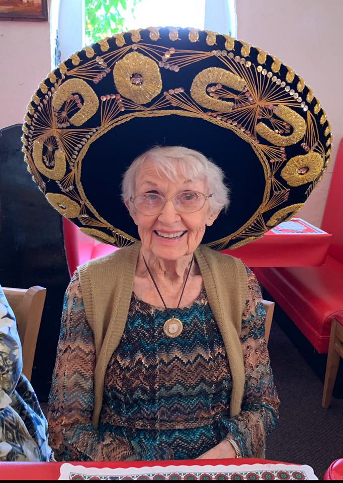 An elderly woman wearing a large sombrero and smiling cheerfully.
