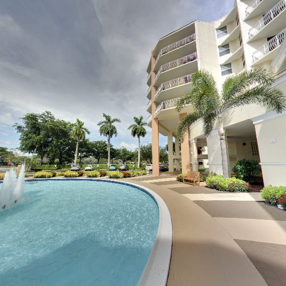A modern building with a swimming pool and palm trees under a cloudy sky.