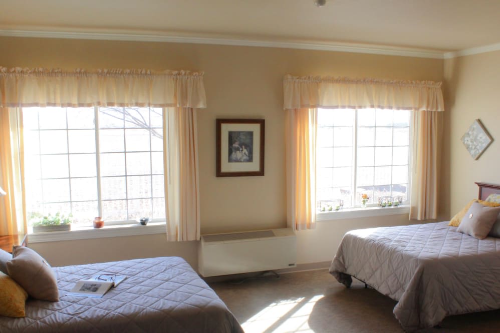 A bright bedroom with two beds and large windows letting in natural light.