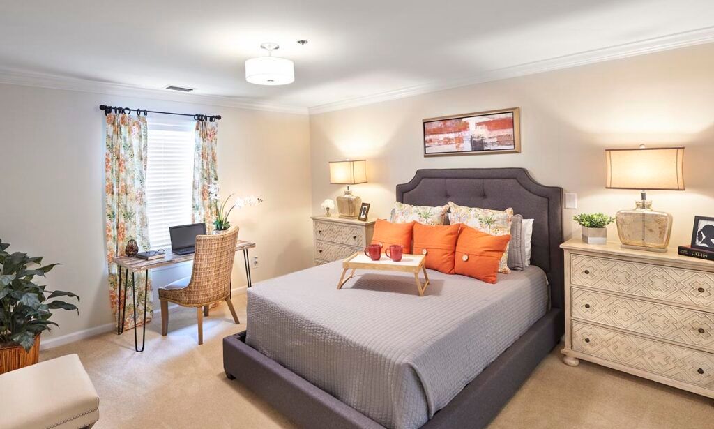 A modern and cozy bedroom featuring a neatly made bed with orange accent pillows and a small desk area beside it.