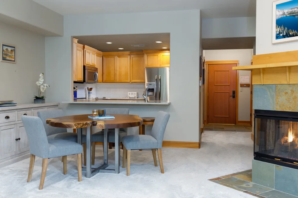 A modern open-plan dining area with a view into the kitchen, featuring wooden furniture and a carpeted floor.