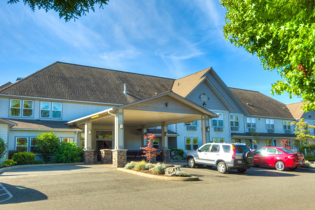 A hotel with a covered entrance and parked cars in the parking lot.