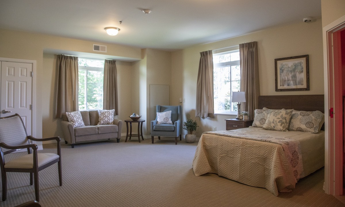 A spacious, cozy bedroom with a bed, sofa, armchair, and large windows allowing natural light.
