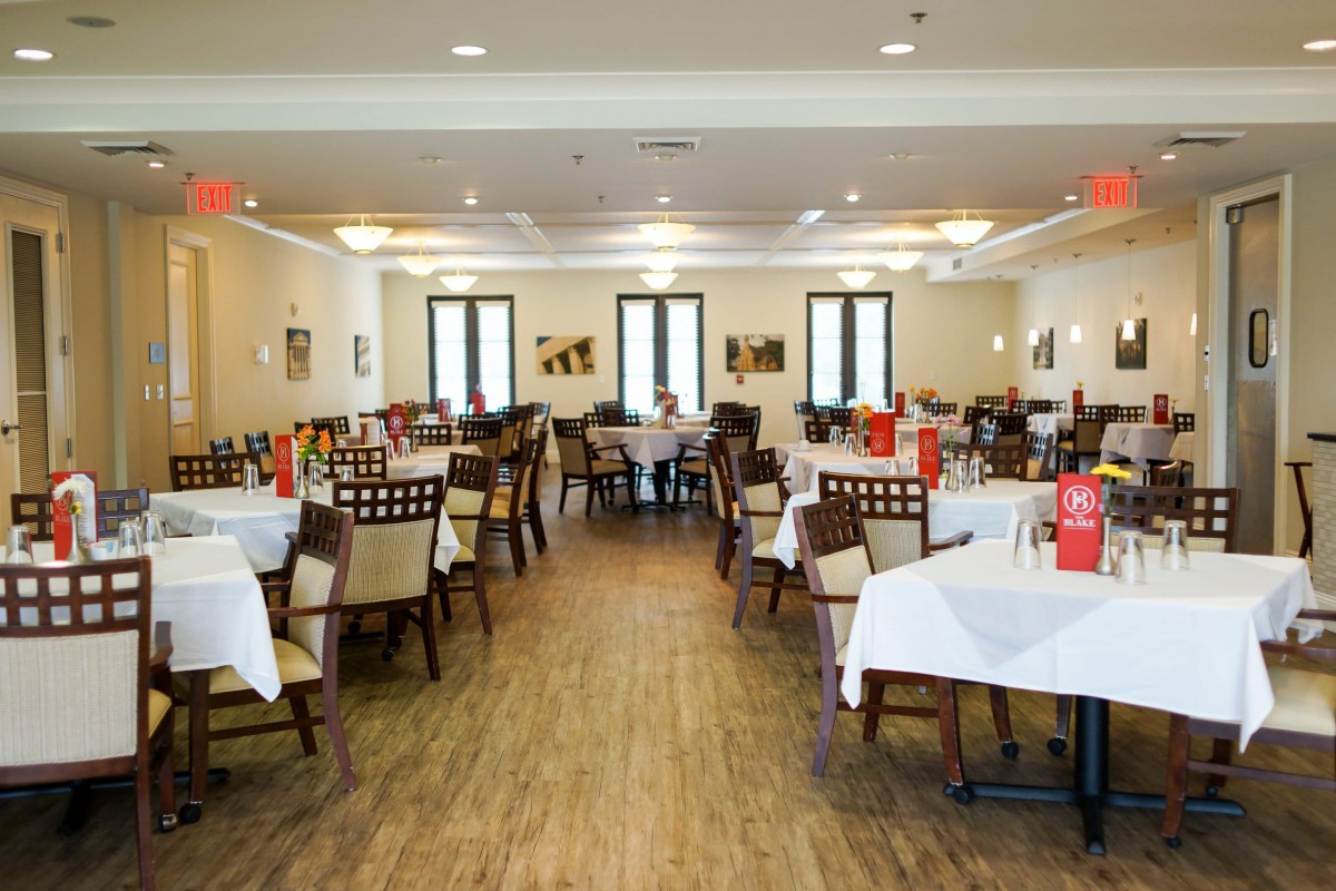 The interior of a restaurant with neatly arranged tables and chairs, adorned with white tablecloths.