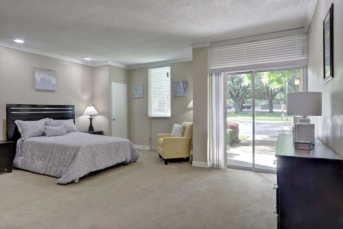 A spacious bedroom with a large bed, cozy chair, and sliding glass doors leading outside.