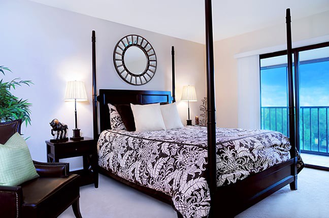 A beautifully decorated bedroom featuring a four-poster bed with patterned bedding, complemented by bedside lamps and a decorative wall mirror.
